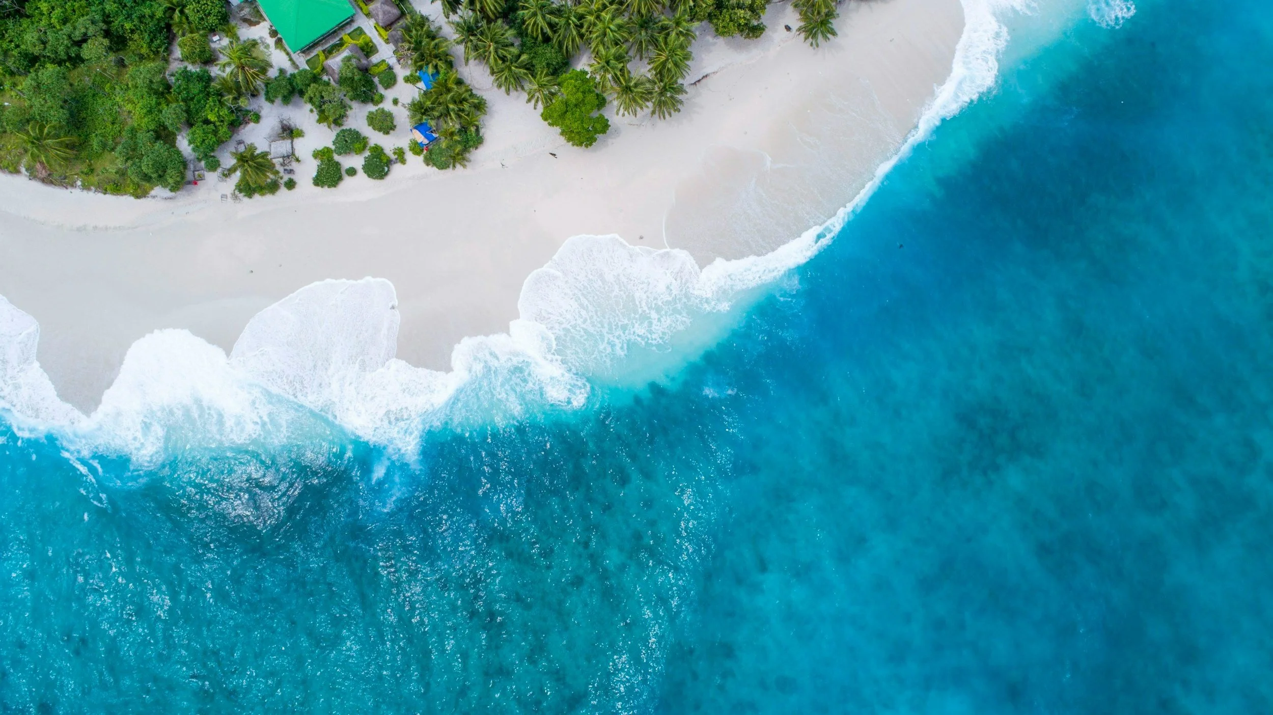 Aerial view of the South Andros shoreline: white sand, turquoise shallows, deep blue beyond